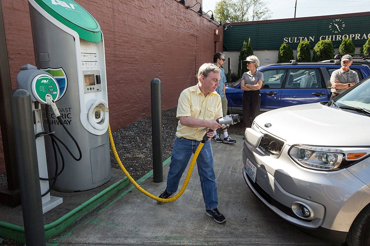 Brian Henderson of Renton plugs in his Kia Soul EV electric vehicle at a charging station in Sultan on in June of 2017. While electric vehicle owners pay a flat fee to the state for transportation needs, they don’t pay a gas tax, which would increase under two proposals in the Legislature (Ian Terry / Herald file photo)