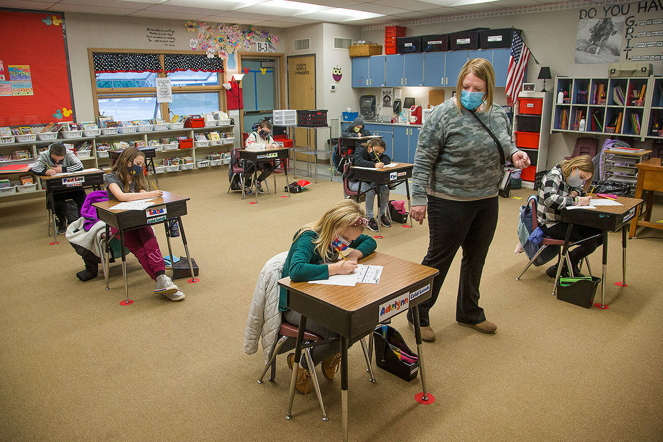 Third grade teacher Lisa Thompson walks by her ten students, separated at six-foot distance, at Eagle Creek Elementary on Wednesday, Jan. 27, 2021 in Arlington, Washington. The students wear masks, are six feet from each other in class and after recess ends, get a mask break. (Andy Bronson / The Herald)