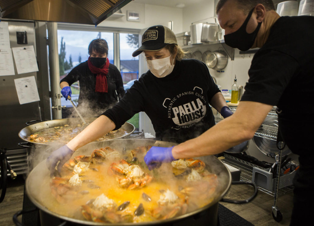 Greg and Laura McLaughlin add mussels to the crab paella they’re cooking in the commercial kitchen in their Snohomish home’s garage. (Olivia Vanni / The Herald)
