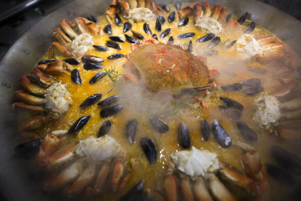 Crab and mussels cook in a large paella pan. Paella means “frying pan” in the Valencian language in Spain. (Olivia Vanni / The Herald)
