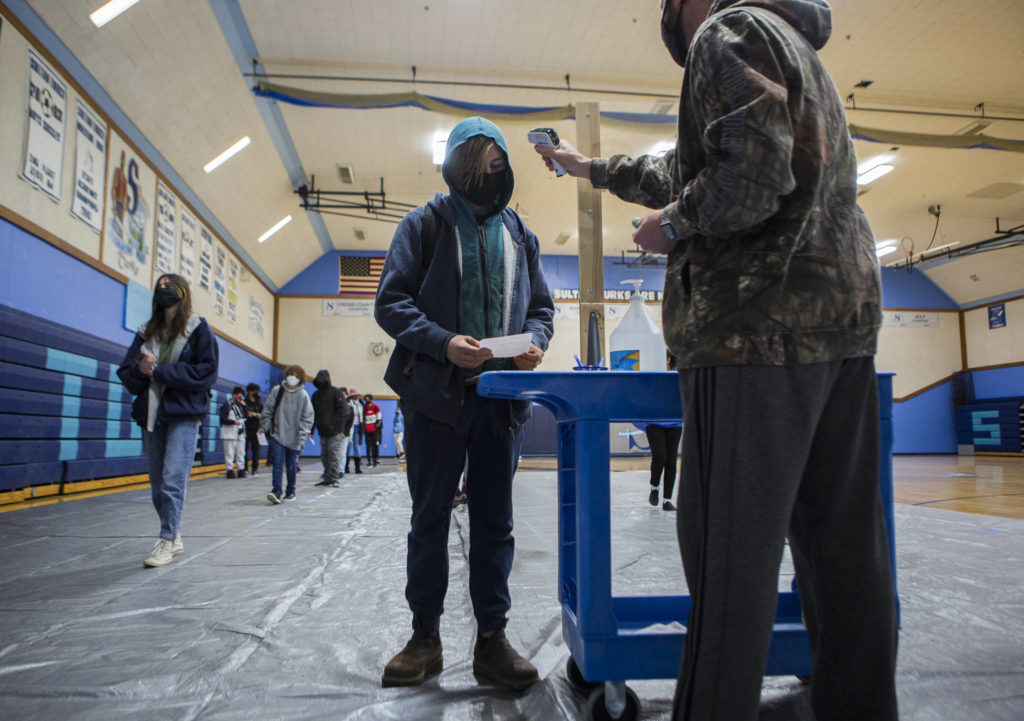 Sultan High School students line up, social distanced, for one of the three temperature and wellness check stations in the gym before classes on Thursday. (Olivia Vanni / The Herald)
