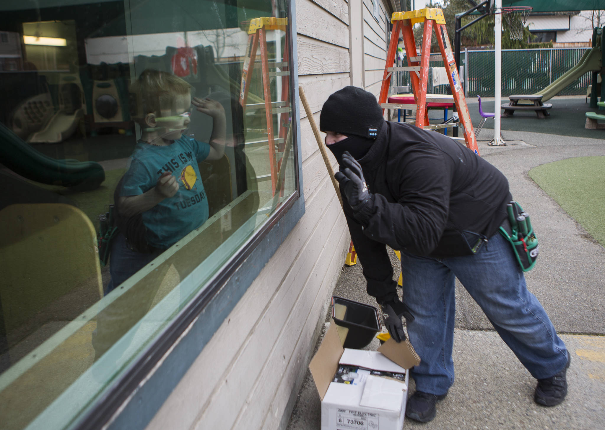 Aaron Perkins, who was trained by HopeWorks programs, is now a maintenance technician for Housing Hope. Here he waves at one of the children in the Tomorrow’s Hope day care in Everett while replacing outdoor light fixtures. (Olivia Vanni / The Herald)