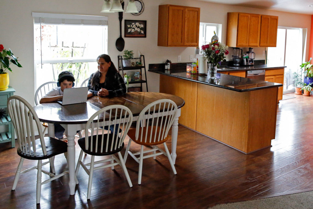 Alma López watches her son Eric Blanquet during remote learning Friday afternoon in Lake Stevens. (Kevin Clark / The Herald)
