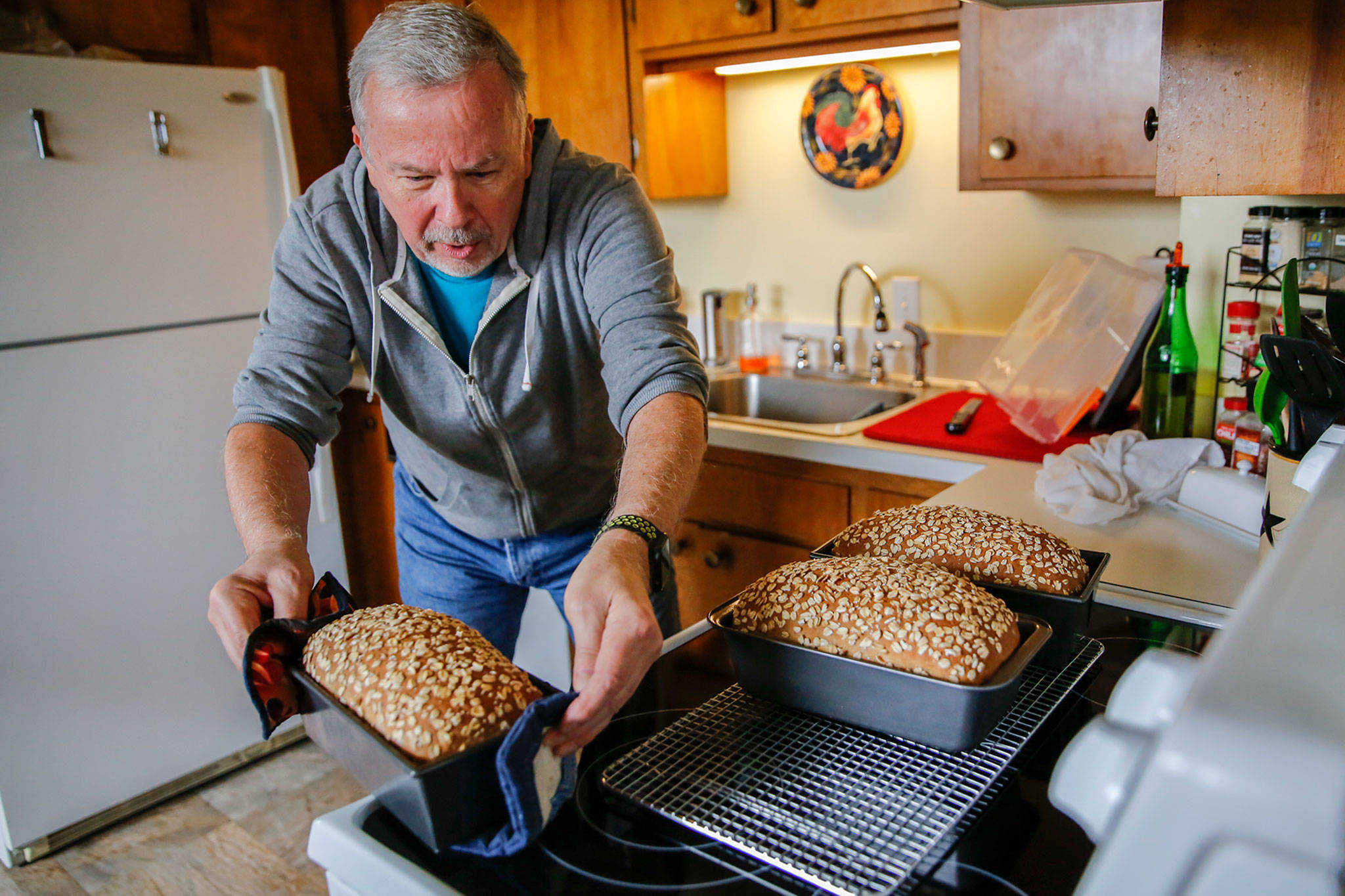 Gerry Betz pulls the finished loaves from the oven Saturday morning at his home in Everett. Betz is the Community Loaves coordinator of the Everett Hub. (Kevin Clark / The Herald)