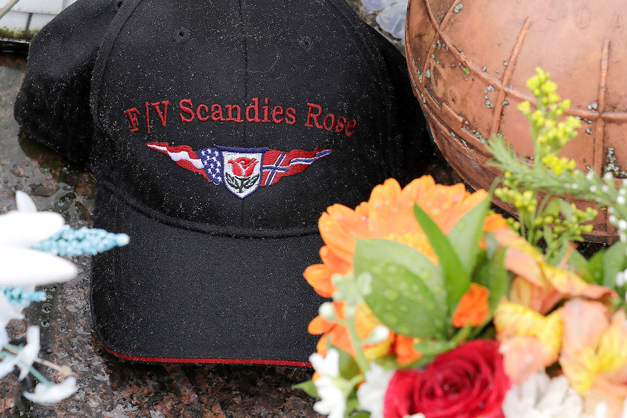 Rain drops gather on a ball cap with the name of the crab fishing boat Scandies Rose, a 130-foot crab fishing boat from Dutch Harbor, Alaska, that sank on New Year’s Eve 2019, as the hat rests near some flowers and a fishing float at the Seattle Fishermen’s Memorial on Jan. 2, 2020, in Seattle. (AP Photo/Ted S. Warren, file)