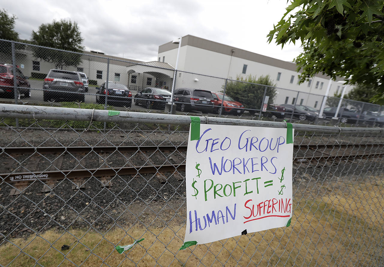 A sign opposing the GEO Group, the private contractor that operates the Northwest Detention Center, hangs on a fence outside the facility in Tacoma on July 10, 2018. (AP Photo/Ted S. Warren, file)