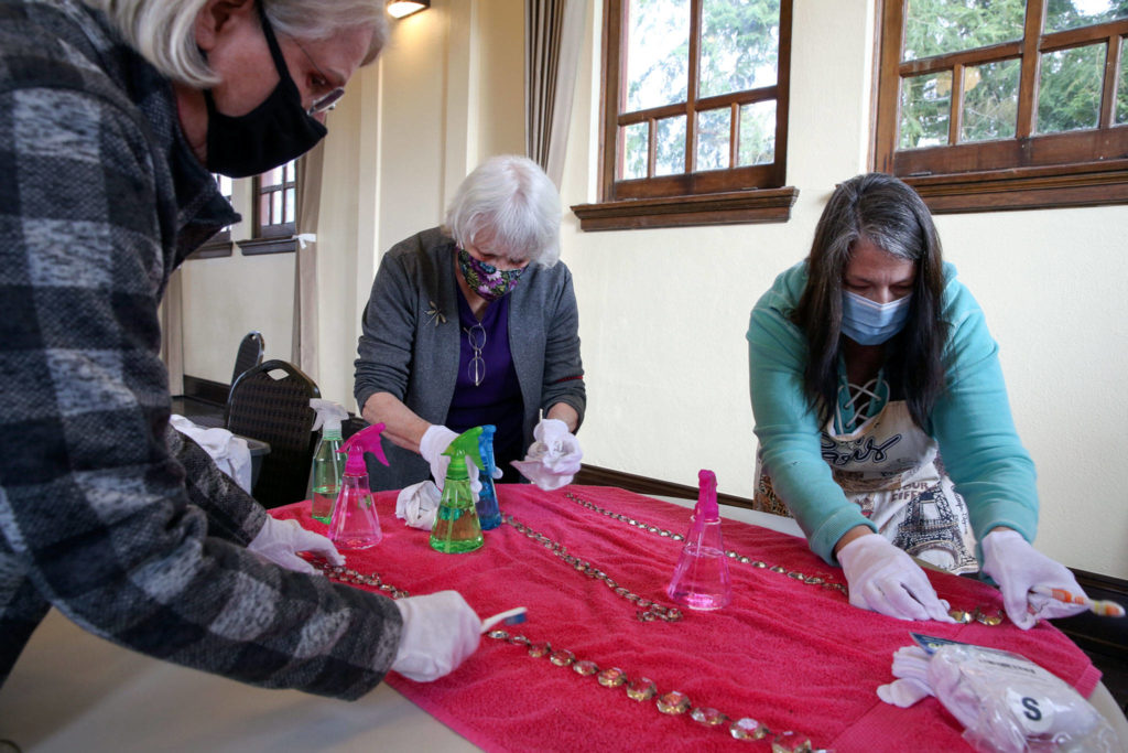 Julie Davis (left), Candice Jarrett (center) and Christine Edwards clean crystals for the reclaimed era chandelier Friday afternoon at the Carnegie Library in Snohomish. (Kevin Clark / The Herald)
