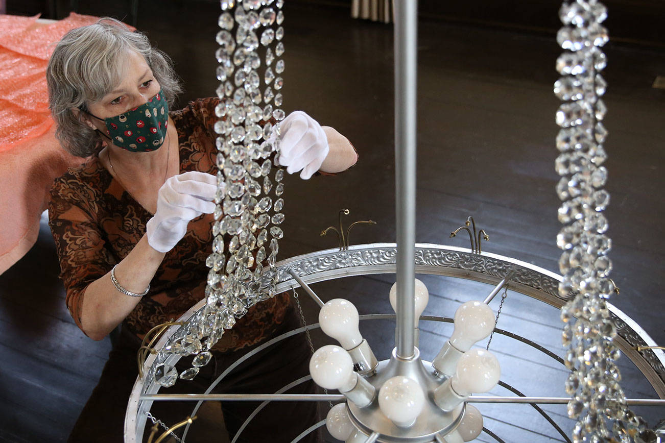 Renee Deierling attaches crystals to the reclaimed era chandelier Friday afternoon at the Carnegie Library in Snohomish on March 26, 2021. (Kevin Clark / The Herald)