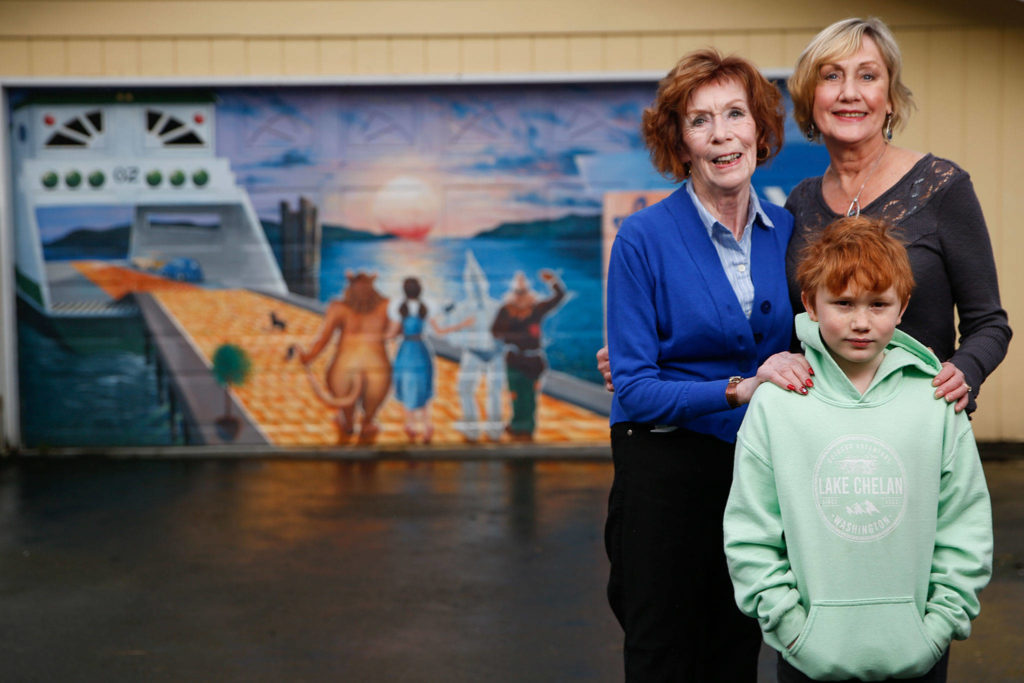 Sharon Pittman, her daughter Diana Jessen and her grandson Xander Pittman, 8, stand in front of a mural on the garage door of her home. It was painted in 2009 by Monroe muralist David Hose in 2009, who has done numerous murals around Snohomish County. (Kevin Clark / The Herald)
