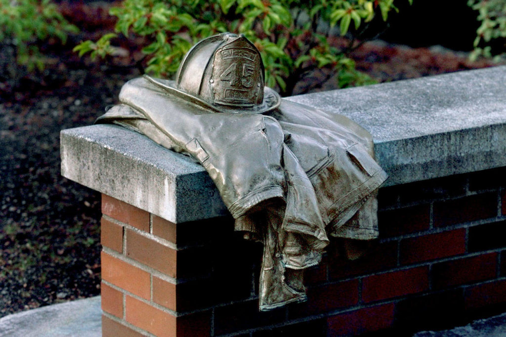A bronze firefighter’s helmet and turnout jacket is mounted on a bench at a Gary Parks memorial outside the Everett Community College library. (Dan Bates / Herald file)
