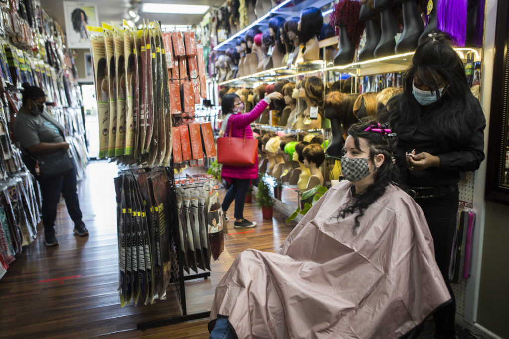 People browse wig and extension options while Decarla Stinn braids Hope Hottemdorf’s hair. (Olivia Vanni / The Herald) 
