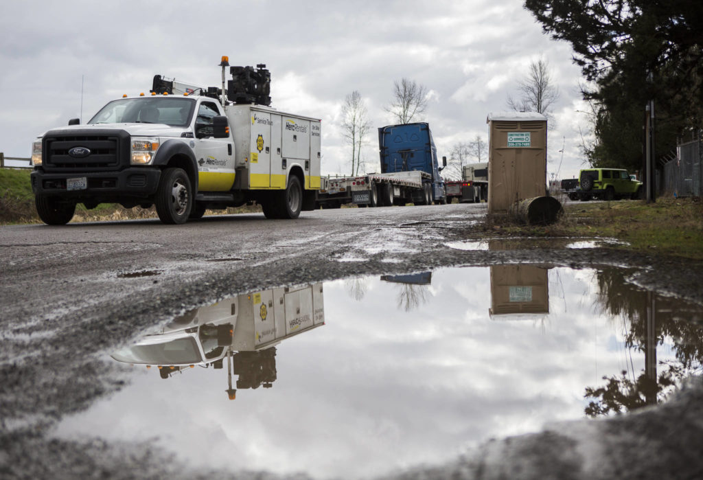 Trucks drive by large puddles and potholes along 40th Avenue NE on Friday in Marysville. (Olivia Vanni / The Herald)
