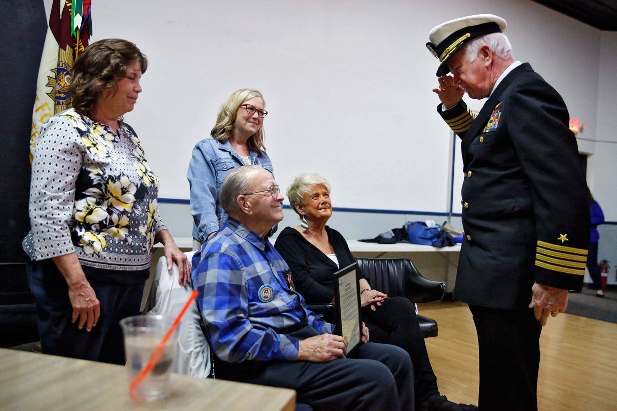 Janet MacDonald (left), Cheri Peterson and Susie Schmidt surround their father, Bob Peterson, a 93-year-old Navy veteran, as he was saluted by Douglas Roulstone, a retired Navy captain who presented Peterson a World War II Victory Medal on Sunday at the VFW in Everett. (Kevin Clark / The Herald)