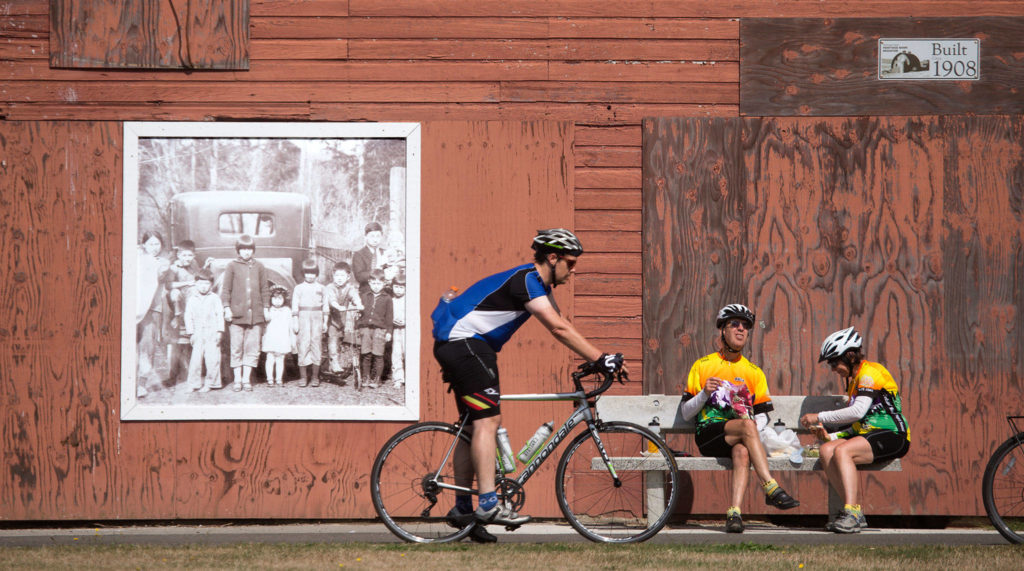 A portrait of the Nakashima family, who were sent to Japanese internment camps during World War II, fades in the sunlight as riders take a break at the Nakashima Barn at the north end of the Centennial Trail in Snohomish County on Sept. 2, 2019 in Arlington. (Andy Bronson / Herald file)
