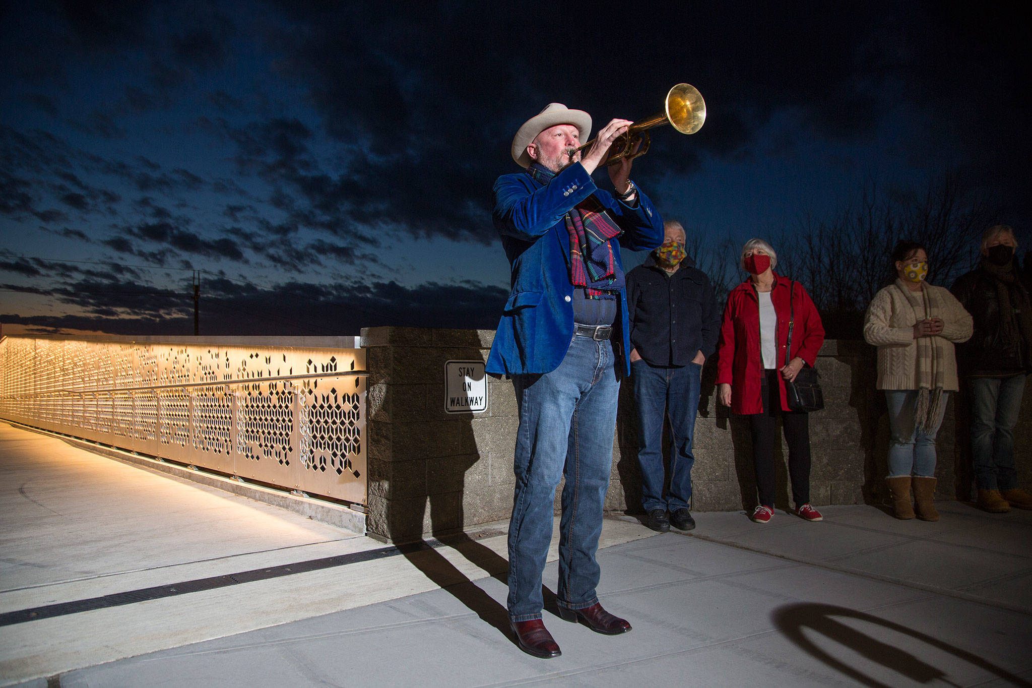 Kevin McKay, who for the past year has been playing Taps from his Everett deck every evening, marks the pandemic year by playing Taps on his horn from the Grand Avenue Park pedestrian bridge on Monday in Everett. (Andy Bronson / The Herald)
