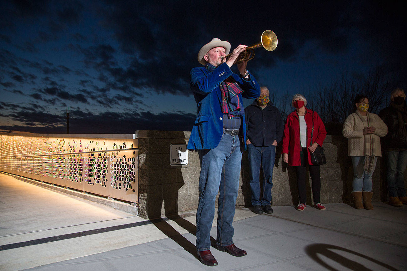 Kevin McKay, who for the past year has been playing Taps from his Everett deck every evening, marks the pandemic year by playing Taps on his horn from the Grand Avenue Park pedestrian bridge on Monday, March 22, 2021 in Everett, Washington.  (Andy Bronson / The Herald)