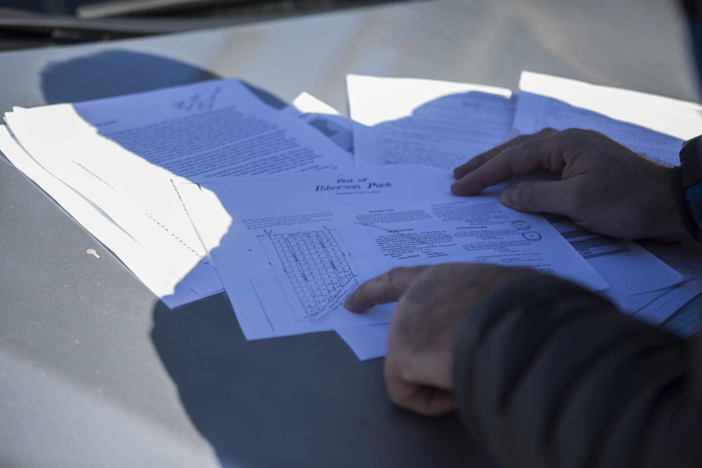 Chris Woytko shows documents that detail ownership of lots along East Ibberson Drive and West Ibberson Drive, a narrow loop along Silver Lake in Everett, on March 10. (Olivia Vanni / The Herald)
