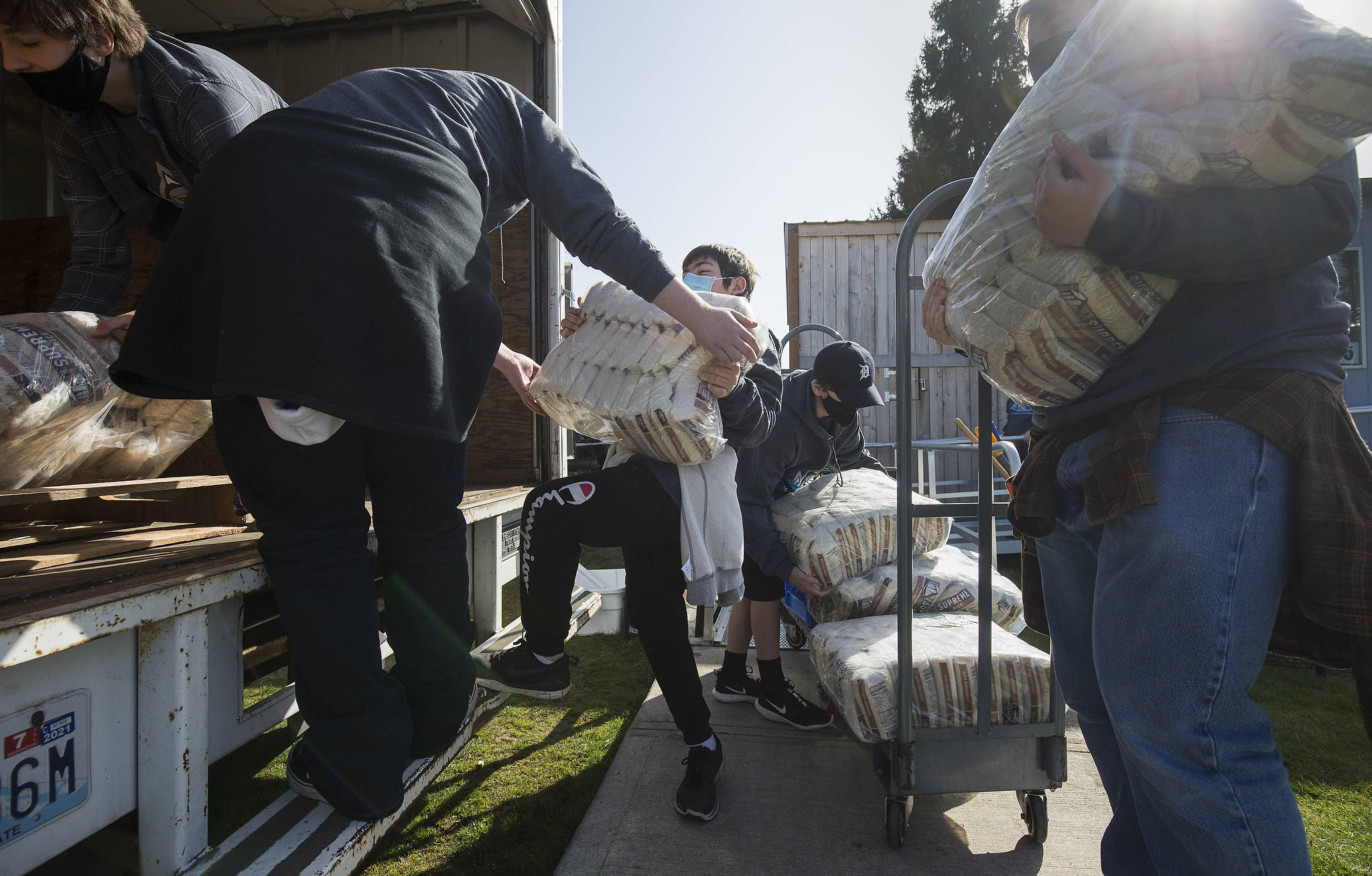 Gabriel van Winkle (center) struggles with lifting a bag of rice weighing nearly half his weight as he and volunteers help move the Granite Falls Food Bank from its old location to a new one Tuesday. (Andy Bronson / The Herald)