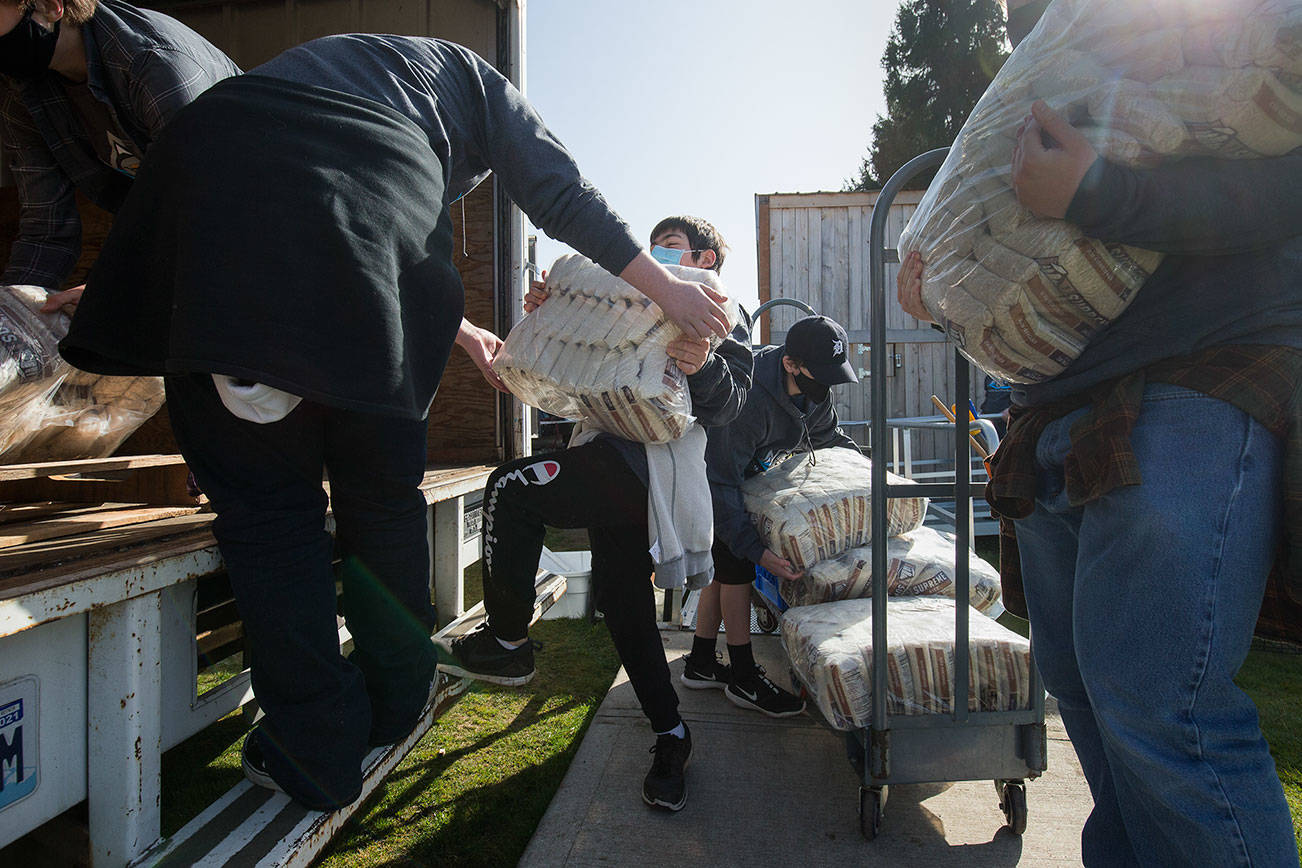 Gabriel van Winkle, center, struggles with lifting a bag of rice weighing nearly half his weight as he and volunteers help move the Granite Falls Food Bank from their old location to a new one on Tuesday, April 6, 2021 in Granite Falls, Washington.  (Andy Bronson / The Herald)