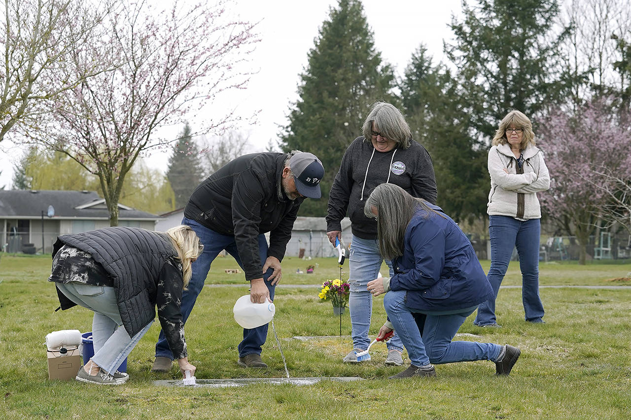 From front left, Wendy Jensen, Joe Woodmansee, Linda Holeman and Bonnie Dawson, the four children of Carole Rae Woodmansee, are joined by family friend Debbie Blazina, at right, March 27, 2021, as they clean the headstone Carole shares with their father, Jim, who died in 2003, at Union Cemetery in Sedro-Woolley. (AP Photo/Ted S. Warren)