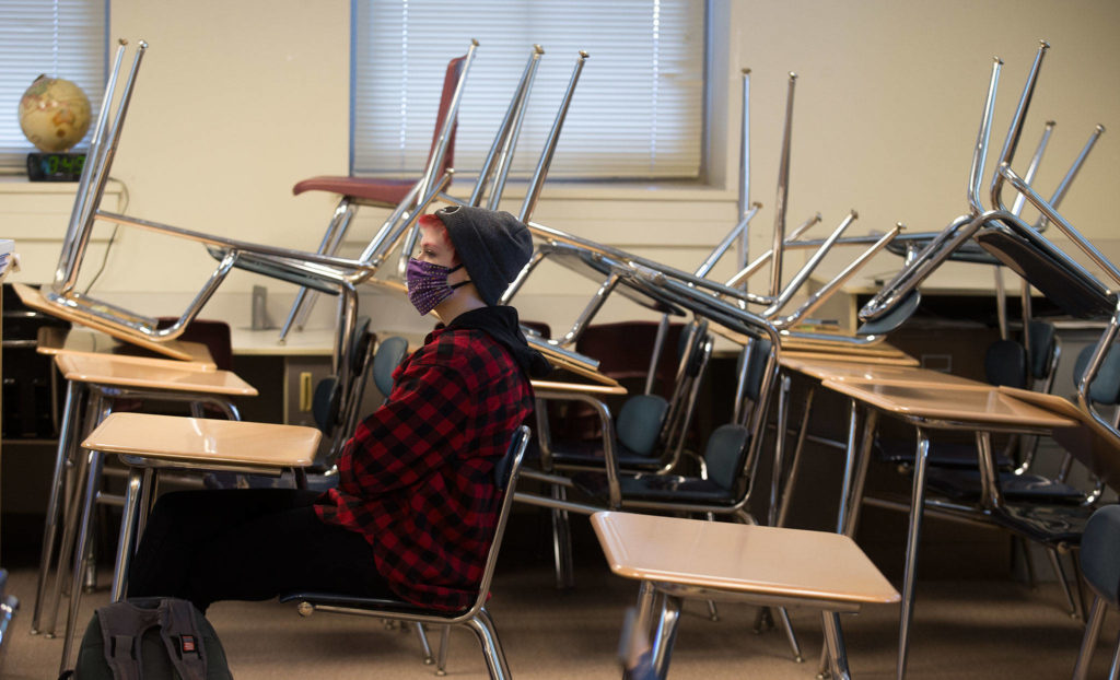With desks stacked to provide room for social distancing, 10th-grader Zendon Bugge attends a world history class during the first day of in-person school for Everett High students on Monday. (Andy Bronson / The Herald)
