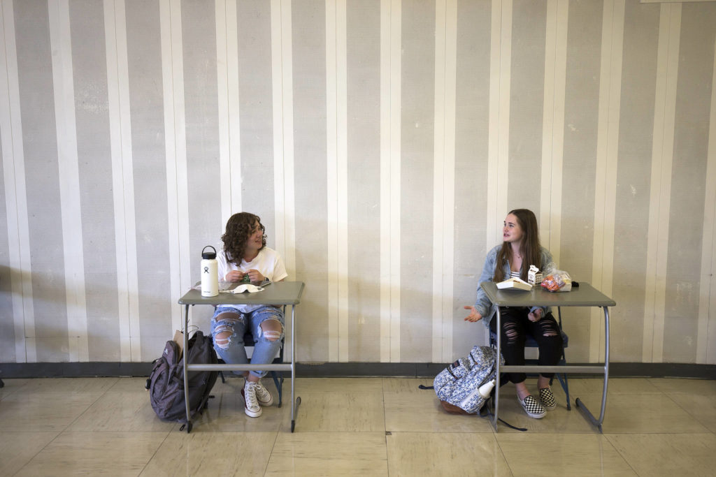Mia Luscher (left) and Makena Limb chat in the cafeteria during the first day of in-person school for Everett High students. (Andy Bronson / The Herald)
