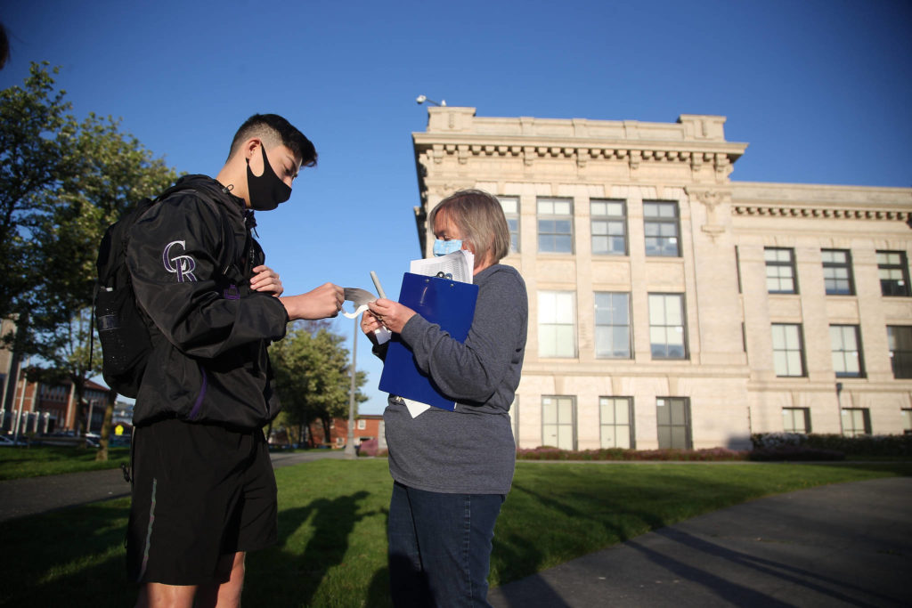 Ryan Sanchez gets a wristband from Barbara Lichneckert on Monday before entering Everett High for the first time this year. (Andy Bronson / The Herald) 
