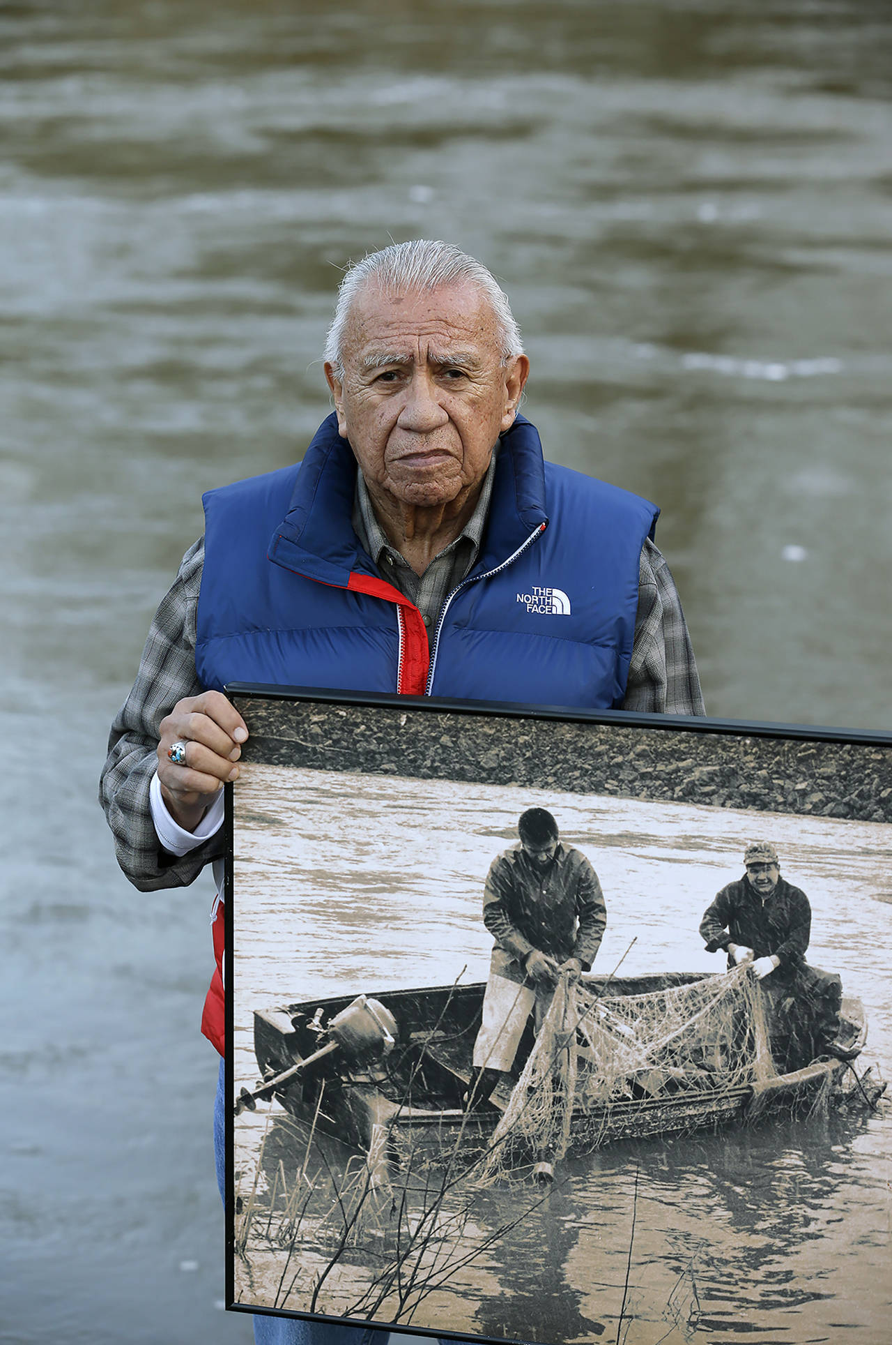 In this Jan. 13, 2014 photo, Billy Frank Jr., a Nisqually tribal elder who was arrested dozens of times while trying to assert his native fishing rights during the Fish Wars of the 1960s and ’70s, holds a 1960s photo of himself (left) fishing with Don McCloud near Frank’s Landing on the Nisqually River. (AP Photo/Ted S. Warren, File)