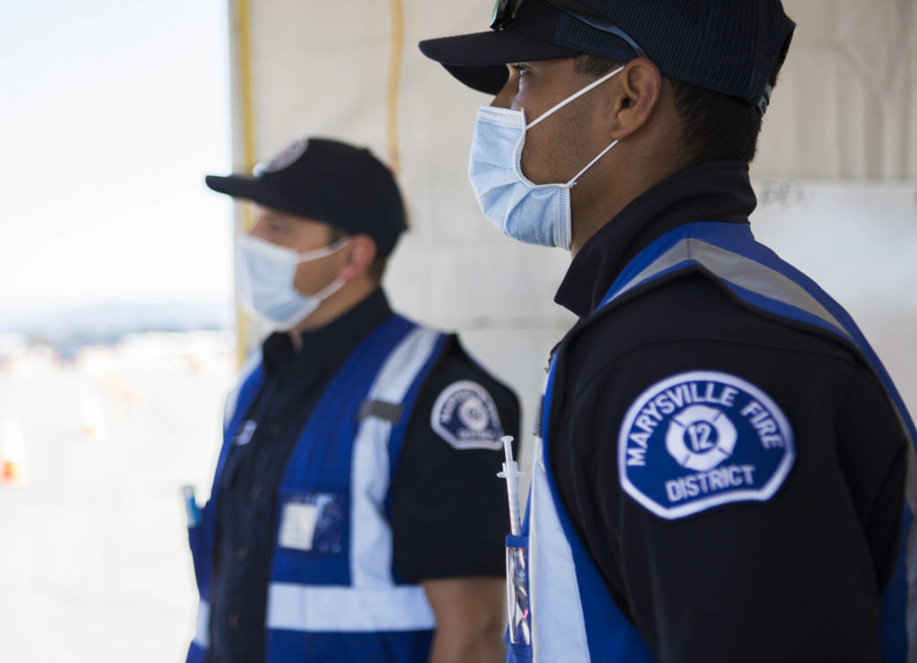 Marysville firefighters listen to Gov. Jay Inslee at the COVID-19 vaccination site at Arlington Municipal Airport on Tuesday. (Olivia Vanni / The Herald)
