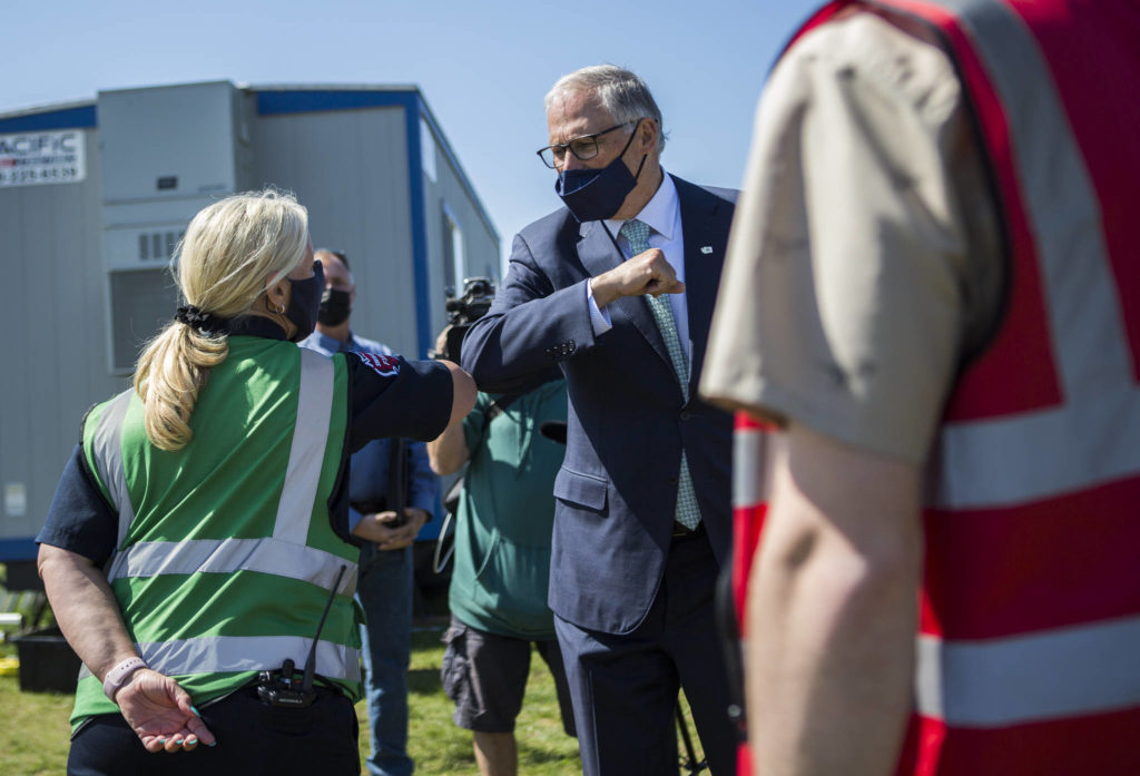 Gov. Jay Inslee greets South County firefighter Nicole Picknell during his visit to the COVID-19 vaccination site at Arlington Municipal Airport on Tuesday. (Olivia Vanni / The Herald) 
