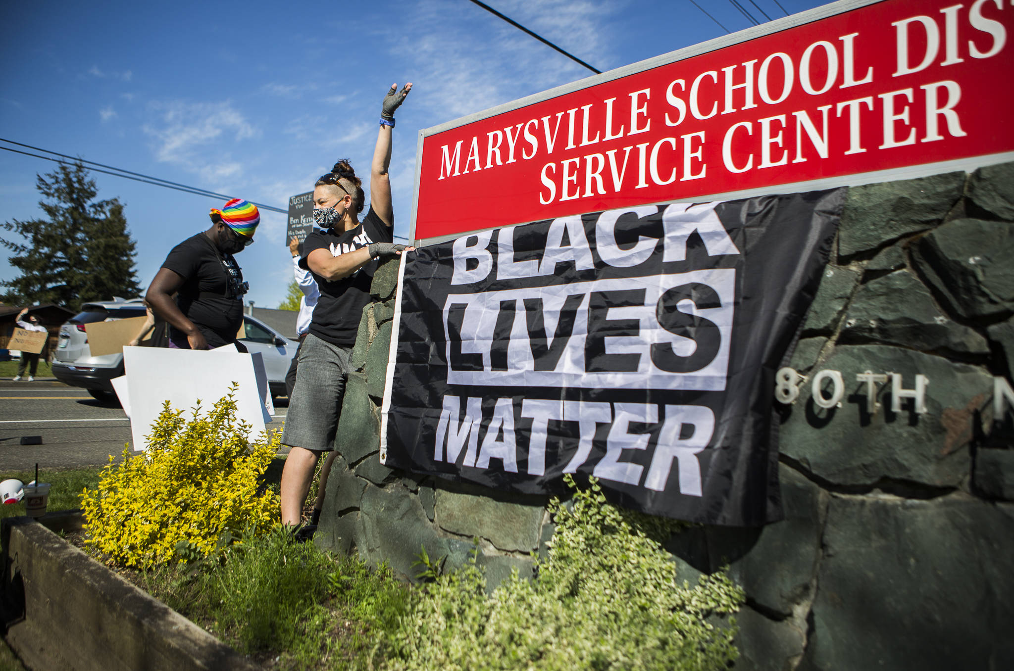 Gus Underfoot hangs a Black Lives Matter flag underneath the Marysville School District sign during a protest on Wednesday. (Olivia Vanni / The Herald)