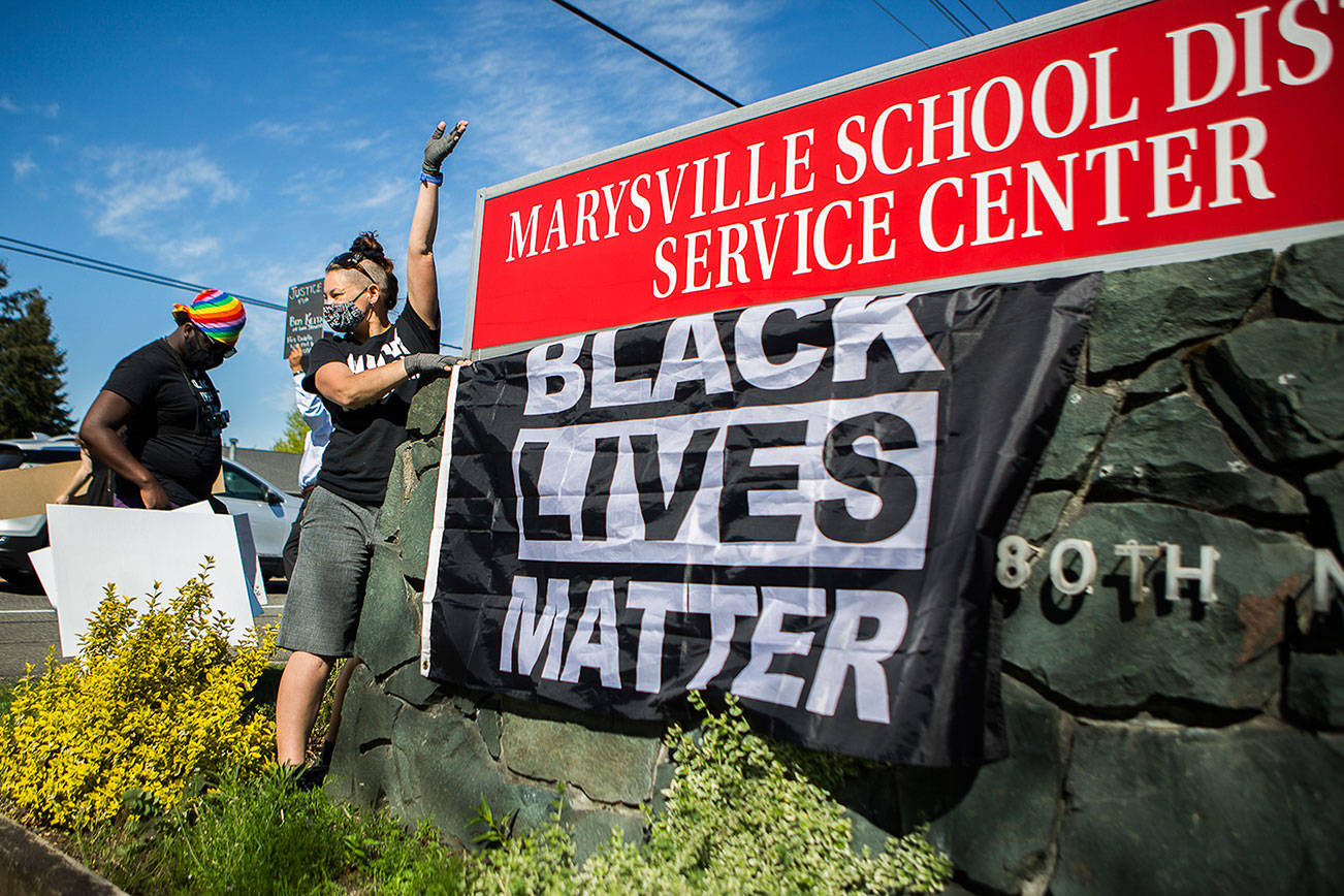 Gus Underfoot hangs a Black Lives Matter flag underneath the Marysville School District sign during a protest on Wednesday, April 21, 2021 in Marysville, Wash. (Olivia Vanni / The Herald)