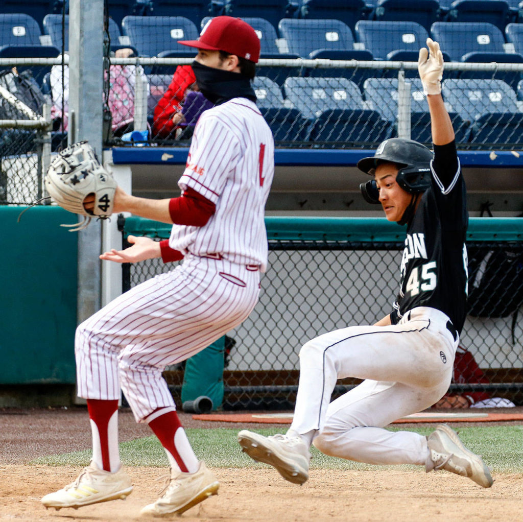 Jackson’s Ryan Nakajima slides safety home with Cascade’s Kam Swartz closing during a game April 23, 2021, at Everett Memorial Stadium. (Kevin Clark / The Herald)
