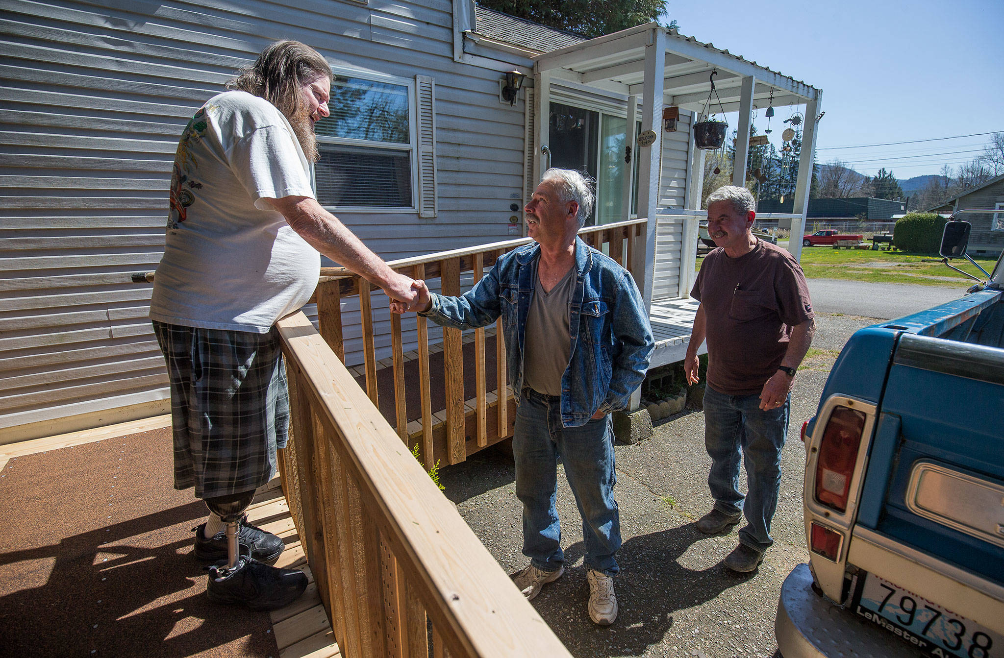 Standing on a new ramp to his home, Doug Waddell shakes hands with Dennis Taylor and Dan Barmon on April 15 in Sultan. Taylor and Barmon built the ramp for Waddell in exchange for two apple pies cooked up by Waddell’s mom and a friend. (Andy Bronson / The Herald)