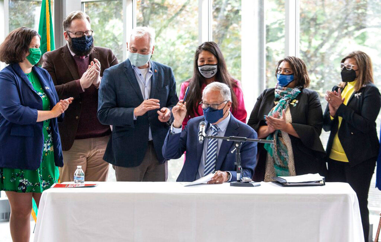 Gov. Jay Inslee signs SB 1050, one of three climate priority bills, including SB 5126 and HB 1091, at Shoreline Community College, May 17, with supporters surrounding him. The triple-bill signing lays out the state’s strategy for combating carbon emissions. (Steve Ringman / The Seattle Times via Associated Press)