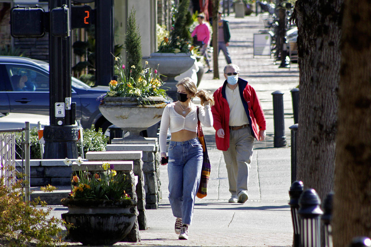 Residents wearing masks walk in downtown Lake Oswego, Ore., in April. Even as the federal Centers for Disease Control and Prevention moved earlier this month to ease indoor face mask-wearing guidance for fully vaccinated people, states like Oregon and Washington are still holding on to certain longtime coronavirus restrictions (Gillian Flaccus / Associated Press)