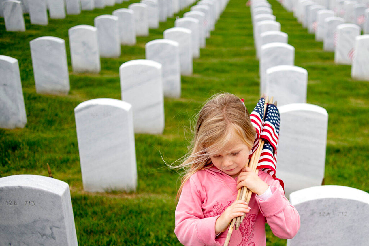 Millie Mester, 5 of Davison, Mich., bows her head as she places American flags at some of the 26,000 headstones, May 27, at the Great Lakes National Cemetery in Holly Township, Mich. Millie and her family joined others volunteering to place an American flag at each headstone before Memorial Day. (Jake May / The Flint Journal via AP)