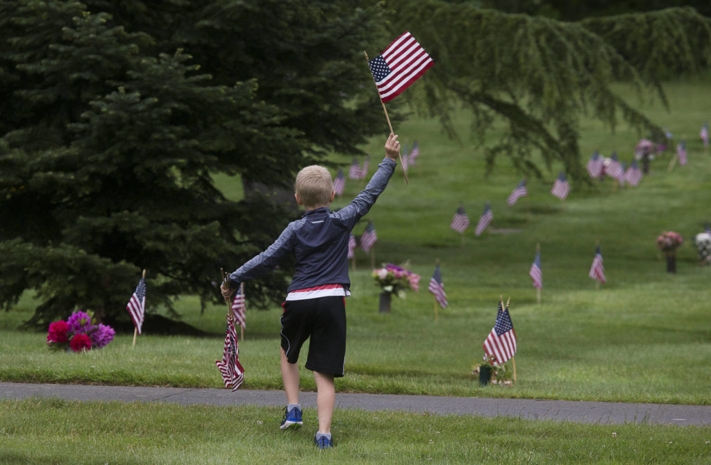 Shane McKenzie, 6, waves a flag as he searches the cemetery for graves without flags, meaning a veteran is buried there, at Floral Hills Cemetery on Memorial Day in 2020 in Lynnwood. (Andy Bronson / The Herald)
