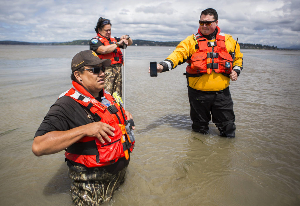 Shawn Edge (left), Robert Guss (center) and Robert Lee McCracken (right) try to locate on a cellphone where Shawn Edge and Charlie Cortez fell in the water, on May 28 in Possession Sound. (Olivia Vanni / The Herald)
