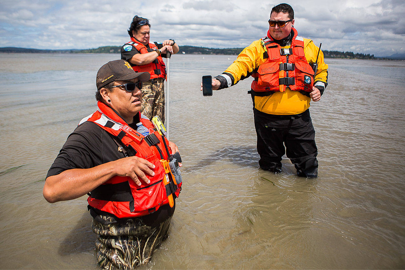 Shawn Edge, left, Robert Guss, center, Robert Lee McCracken, right, try to locate on a cellphone where Shawn Edge and Charlie Cortez fell in the water on Friday, May 28, 2021 in Possession Sound, Wash. (Olivia Vanni / The Herald)