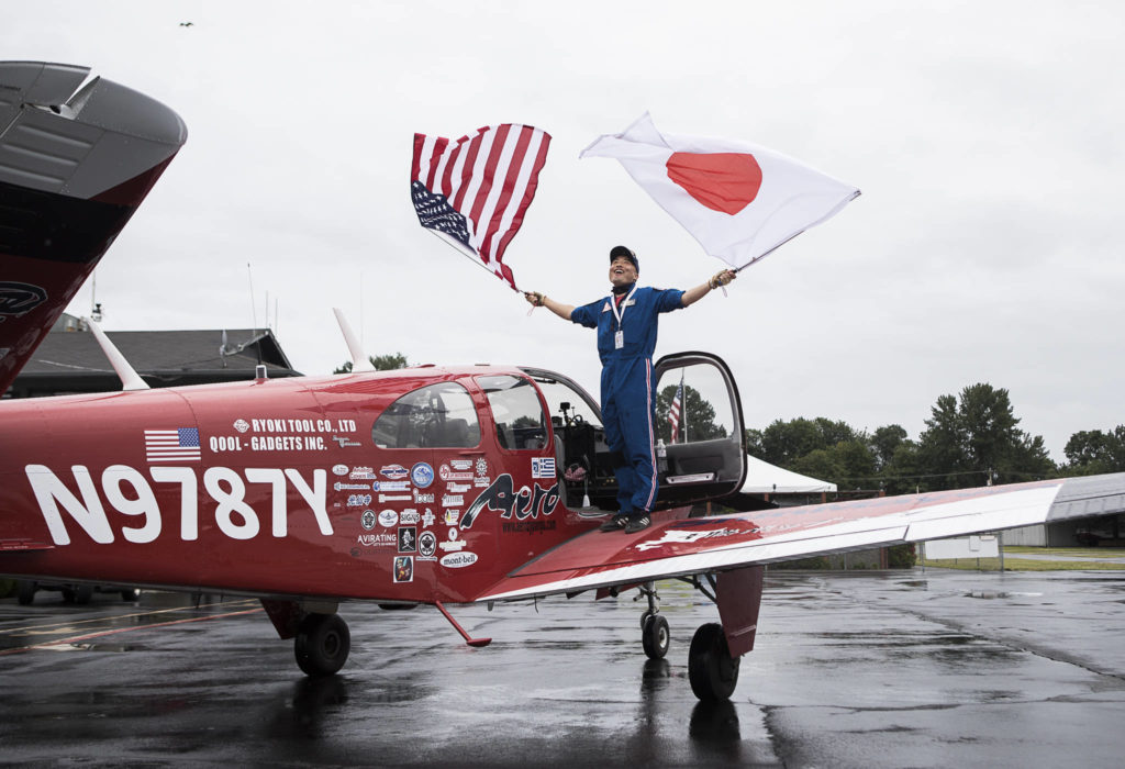 Shinji Maeda steps out of his plane on Friday in Snohomish, waving American and Japanese flags after completing his round-the-world tour, which took him to 18 countries. (Olivia Vanni / The Herald)
