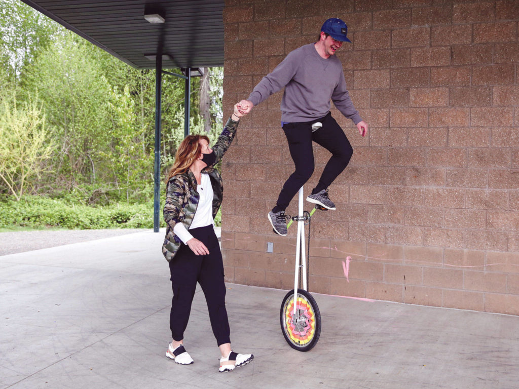 Toni Munizza helps Nate Feltner ride the “giraffe” unicycle. (Kevin Clark / The Herald) 

