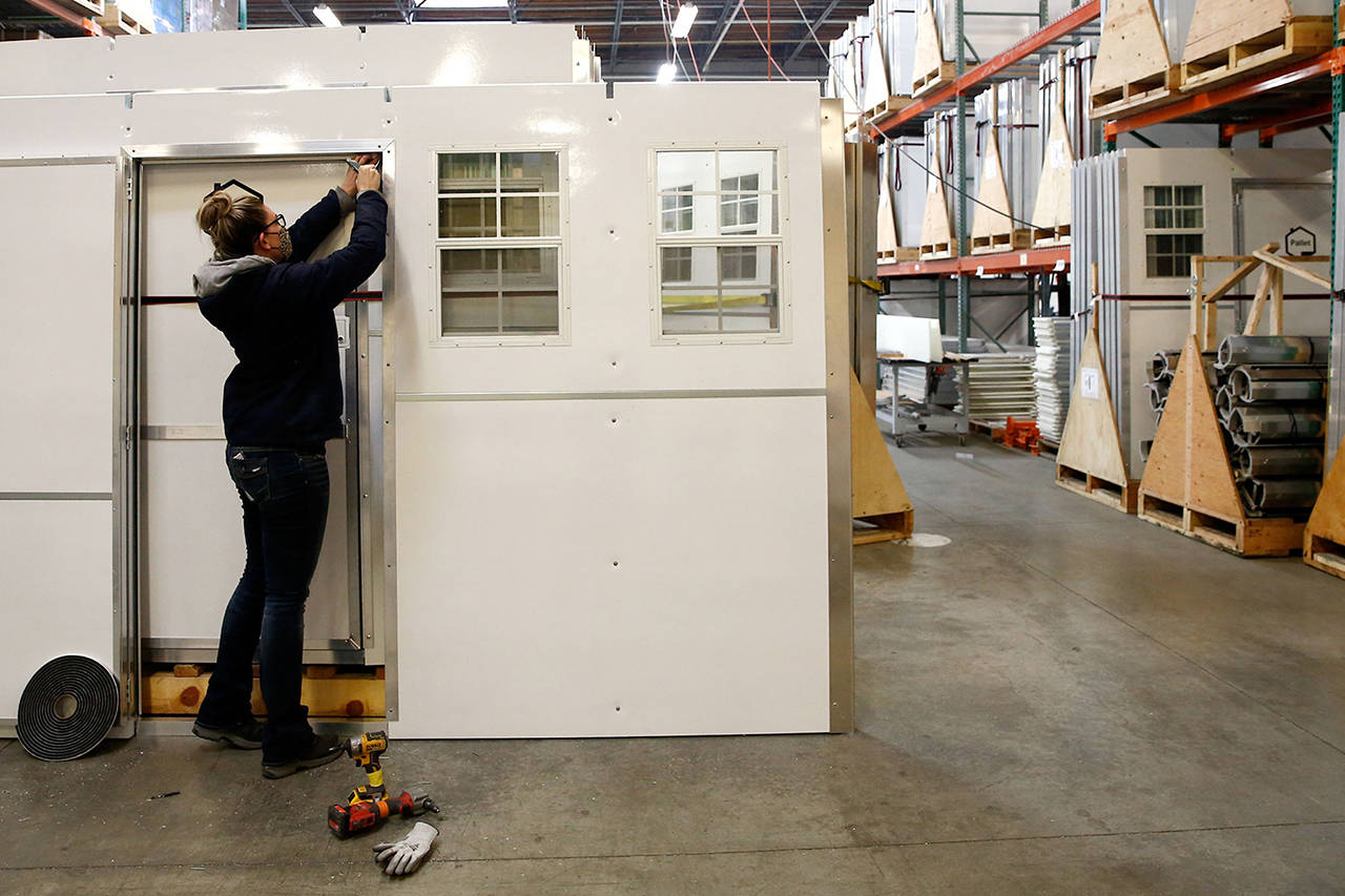 Tiny-home communities are groups of small shelters for unhoused people. Here a worker installs weatherstripping on a pallet shelter at Pallet in Everett in 2020. (Kevin Clark / Herald file)