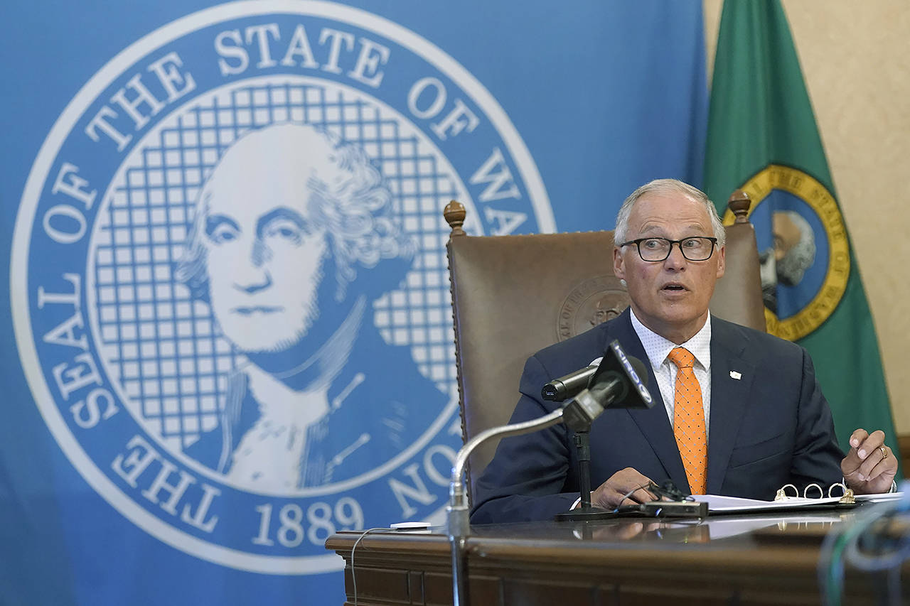 Washington Gov. Jay Inslee glances at an aide holding up an image of a visual slide being shown to viewers of a June 3 news conference in Olympia. (AP Photo/Ted S. Warren, file)