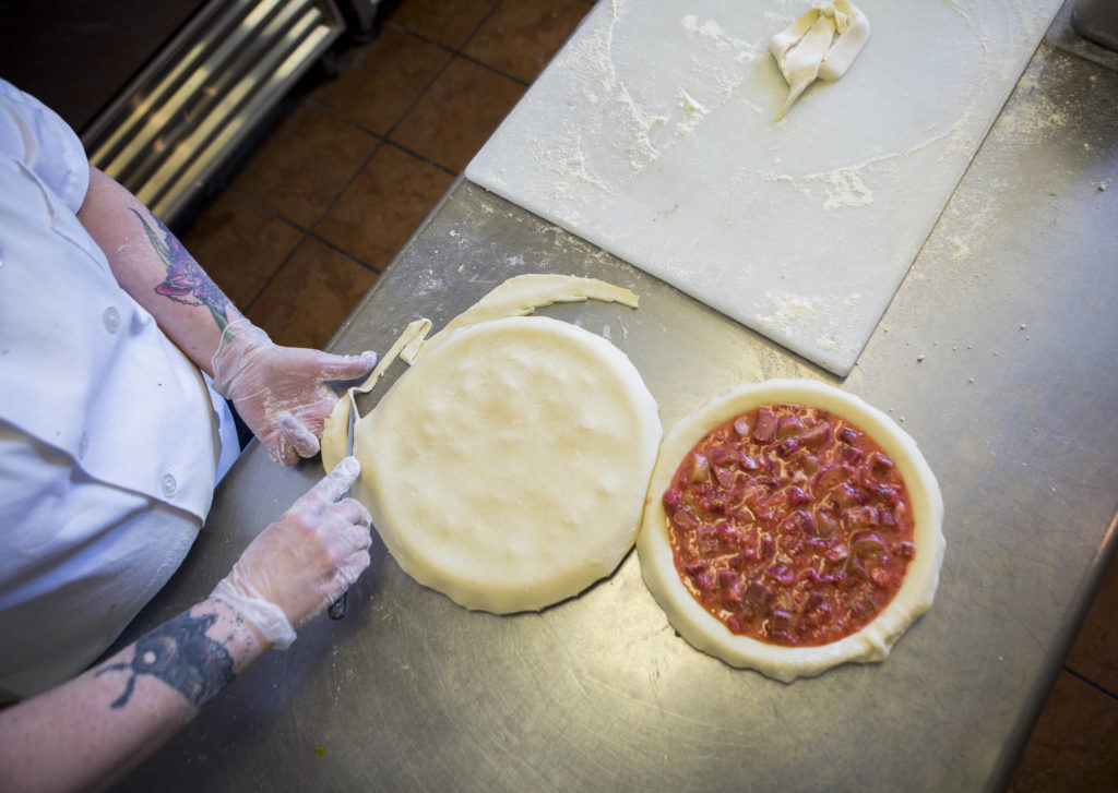 Cheryl Olsen trims the crust off a strawberry rhubarb pie at Village Taphouse and Grill in Marysville. (Olivia Vanni / The Herald)
