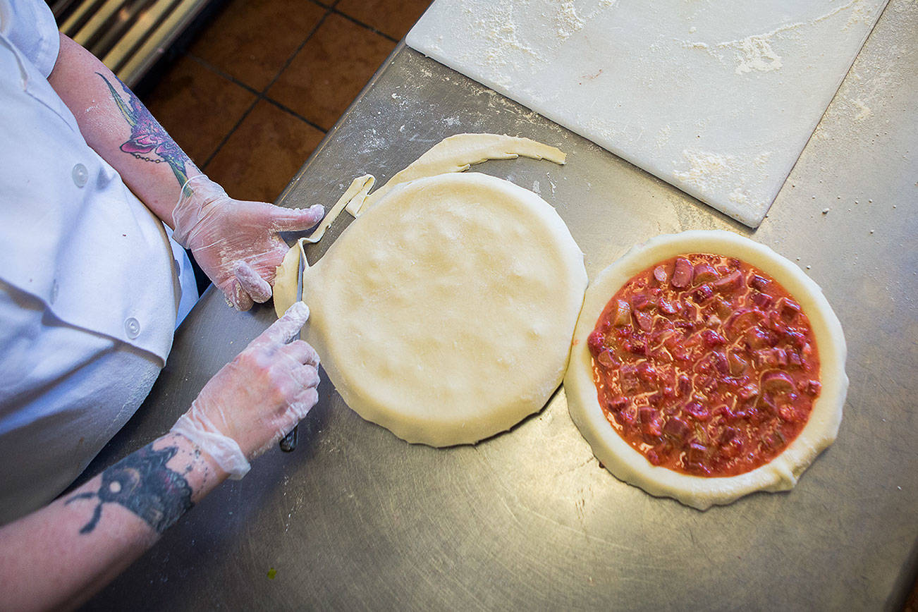 Cheryl Olsen trims the crust off a strawberry rhubarb pie at Village Taphouse and Grill in Marysville. (Olivia Vanni / The Herald)