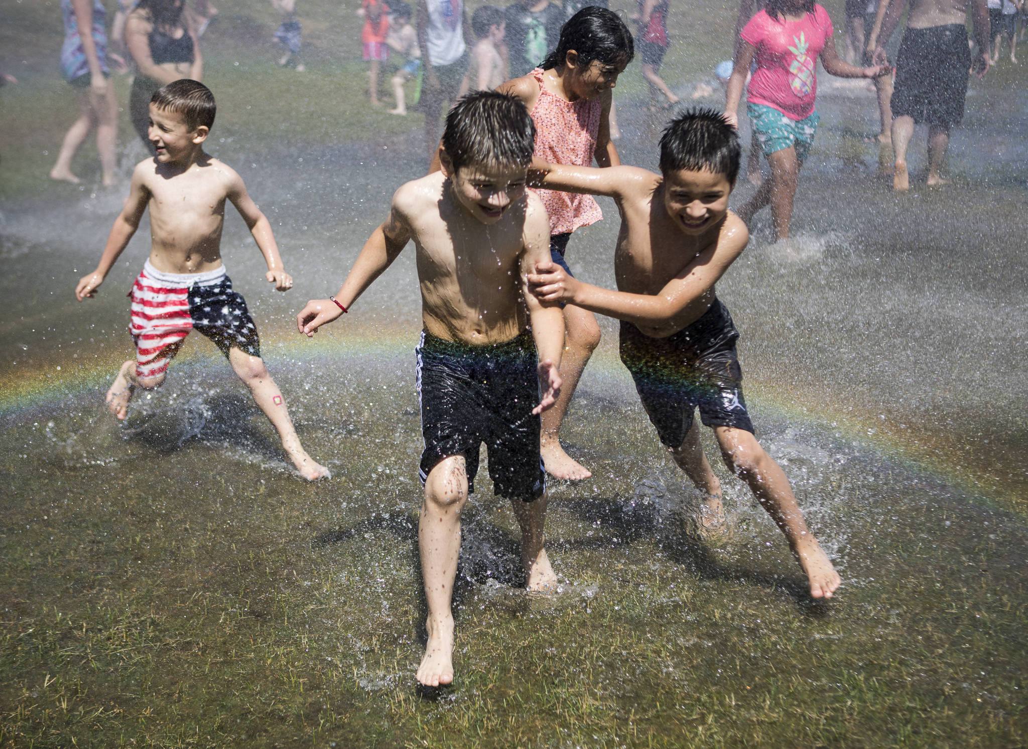 David Parada, 7, left, and Abel Parada, 8, run through a heavy spray of water creating a rainbow Saturday at Walter E. Hall Parkin Everett. The Everett Fire Department set up a fire hose sprinkler station to help people cool down and escape the heat. (Olivia Vanni / The Herald)