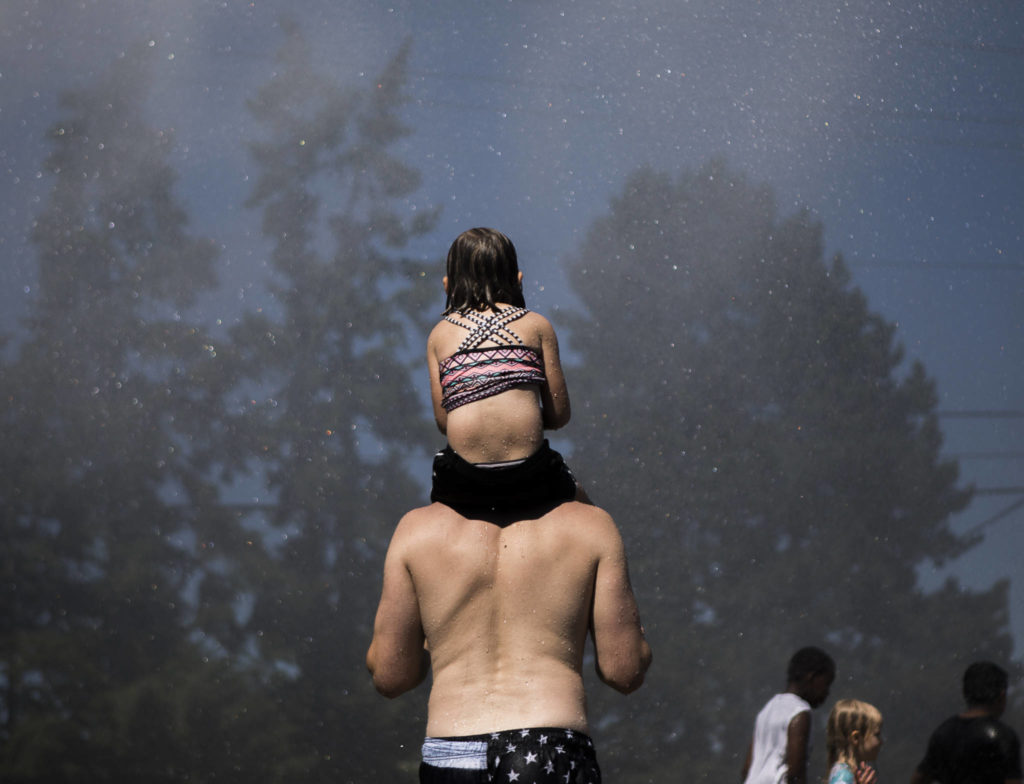 People stand in the spray from the Everett Fire Department’s fire hose sprinkler station Saturday at Walter E. Hall Park in Everett. (Olivia Vanni / The Herald)
