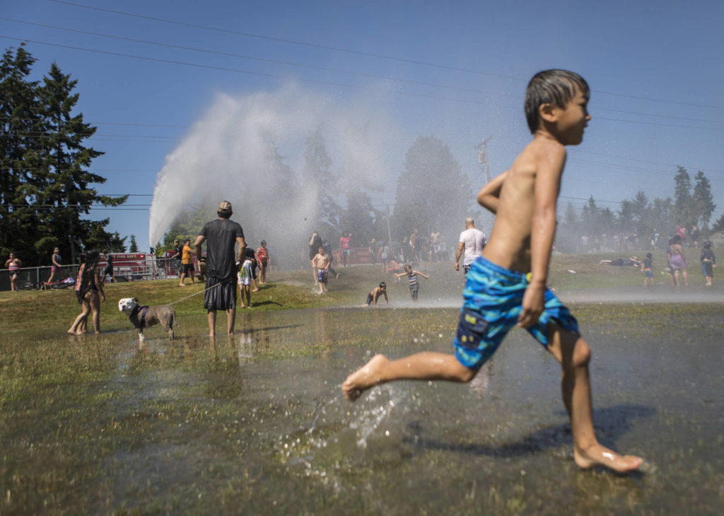 People enjoy the fire hose sprinkler station set up Saturday by the Everett Fire Department at Walter E. Hall Park in Everett. (Olivia Vanni / The Herald)
