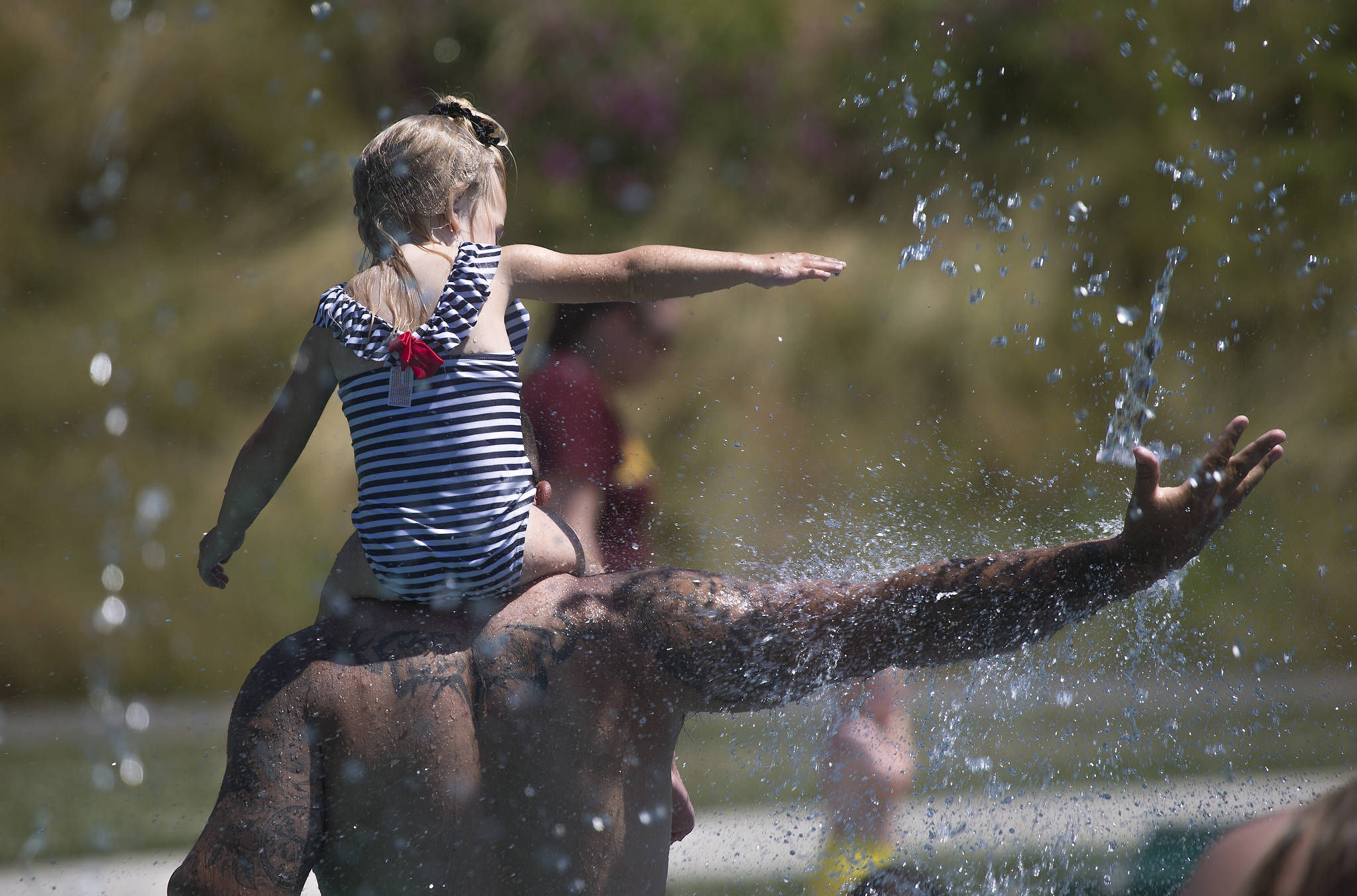Keeping cool in record setting heat, Beau Jess and daughter River, 3, reach for falling water as they play at the Splash Pad in Haller Park on Monday in Arlington. (Andy Bronson / The Herald)